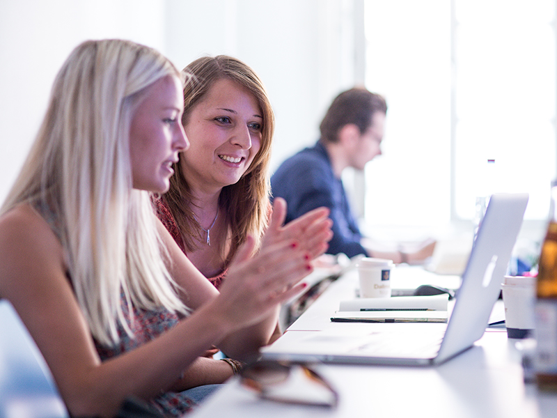 Zwei Studierende sitzen an einem Laptop und unterhalten sich