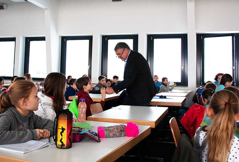 Kinder sitzen an Tischen, Prof. Luppold zwischen den Gängen mit Mirko