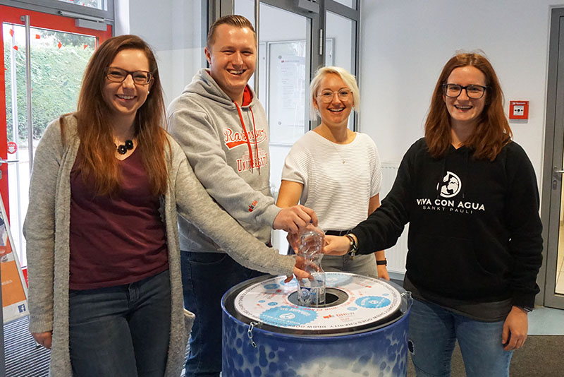 Cramer, Browski, Mögle und Roth halten eine Pfandflasche in eine Tonne