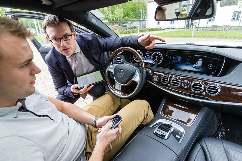 Student und Professor begutachten den Bordcomputer eines Mercedes