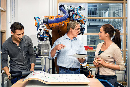 Studentin und Student mit Dozent vor einem Roboter