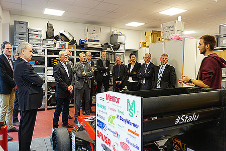 Dozierende hören Student zu, der neben dem DHBW-Rennwagen steht