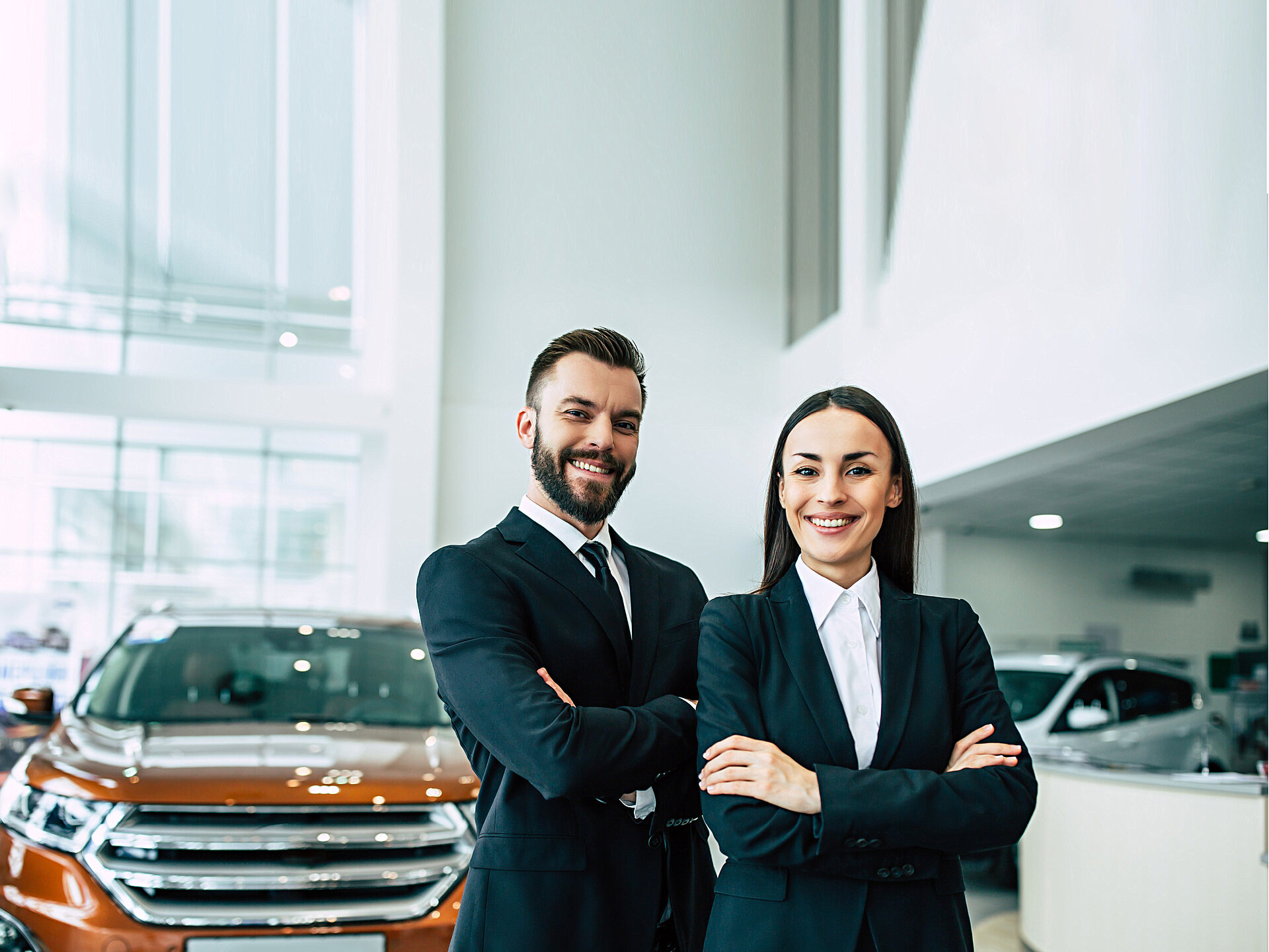 Zwei Autohändler stehen mit verschränkten Armen lächelnd in einem Autohaus