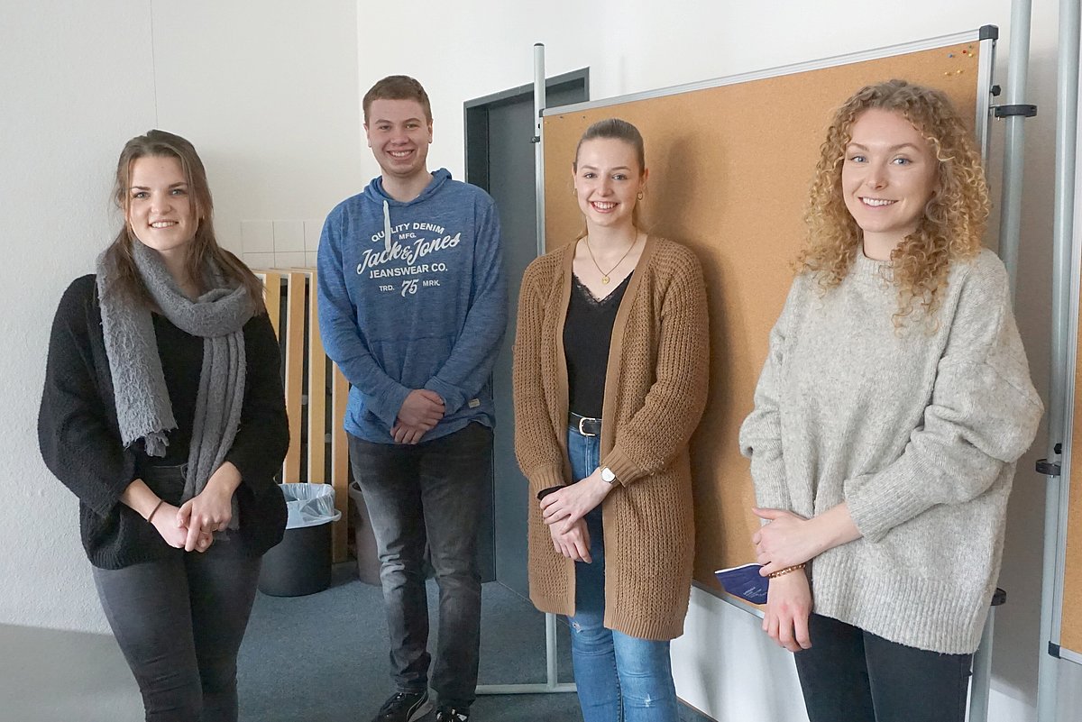 Vier DHBW-Studierende stehen lächelnd vor einer Stellwand.
