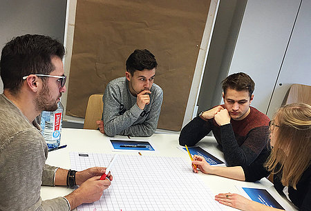 Vier Studierende sitzen um einen Tisch und arbeiten gemeinsam
