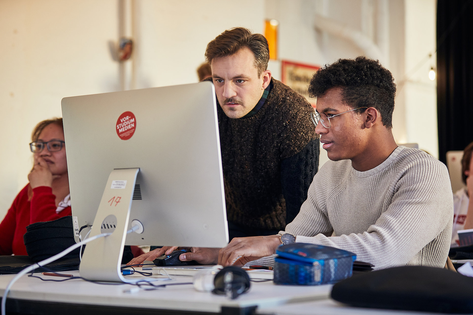 Professor erklärt Student etwas an einem MAC