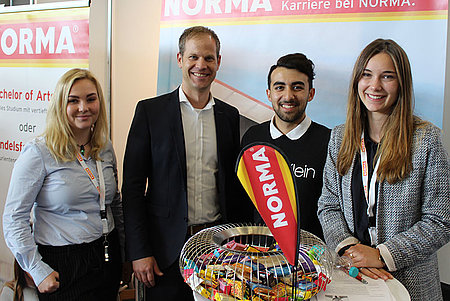 Personalchef von Norma mit drei Studierenden auf dem Norma-Ausbildungsstand