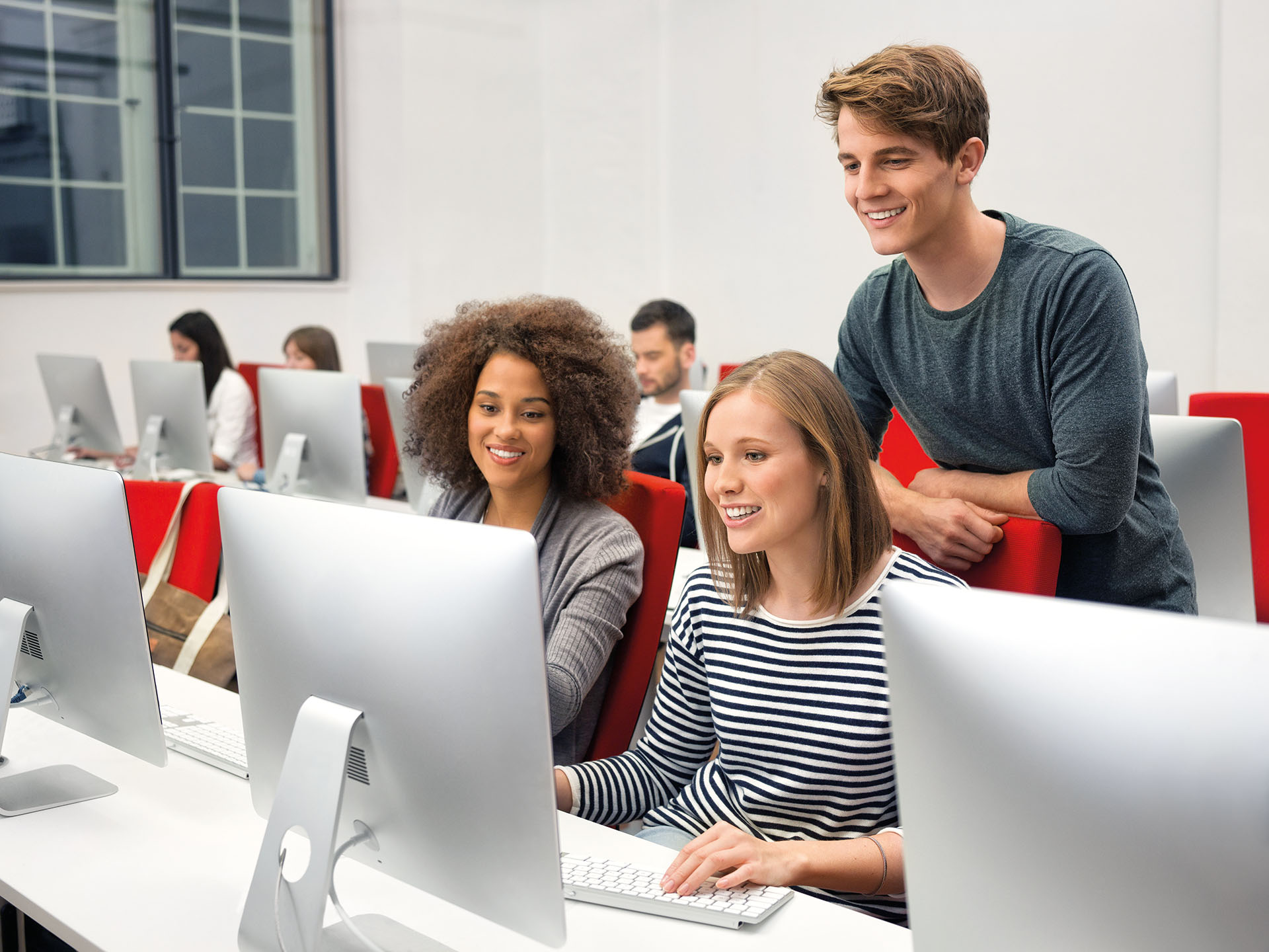 Zwei Studentinnen und ein Student sitzen vor einem Rechner in einem Mac-Labor.